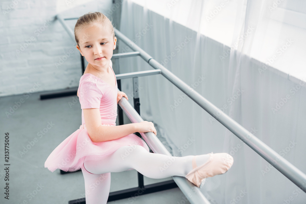 adorable kid in pink tutu stretching and practicing in ballet school