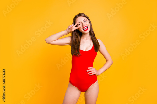 Party mood! Portrait of foolish playful girl gesturing v-sign near winking eye showing tongue out looking at camera isolated on vivid yellow background