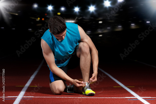 young athletic male sitting on running track and stretching at sports stadium photo