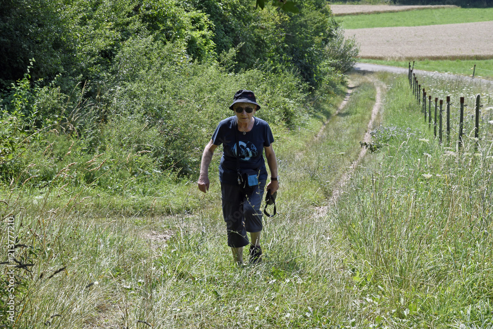 eine seniorin geht auf einem feldweg eine seniorin geht auf einem feldweg