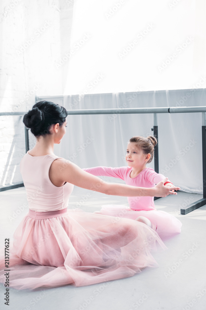 Naklejka premium young ballet teacher and little student in pink tutu skirts training together in ballet school