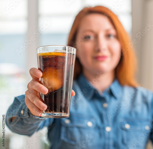 Redhead woman holding soda refreshment with a confident expression on smart face thinking serious