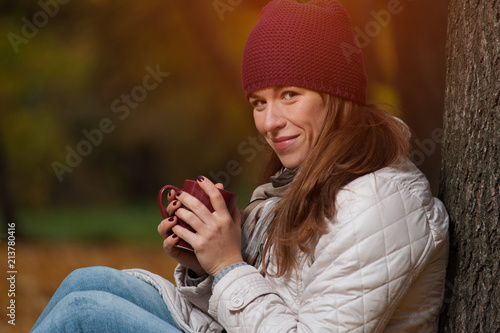 Beautiful young woman drinking tea in fall nature background. Autumn concept