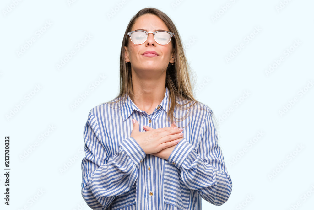 Beautiful young woman wearing elegant shirt and glasses smiling with hands on chest with closed eyes and grateful gesture on face. Health concept.