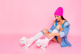 Attractive girl in stockings on roller skates ties up the shoelaces isolated on bright pink background