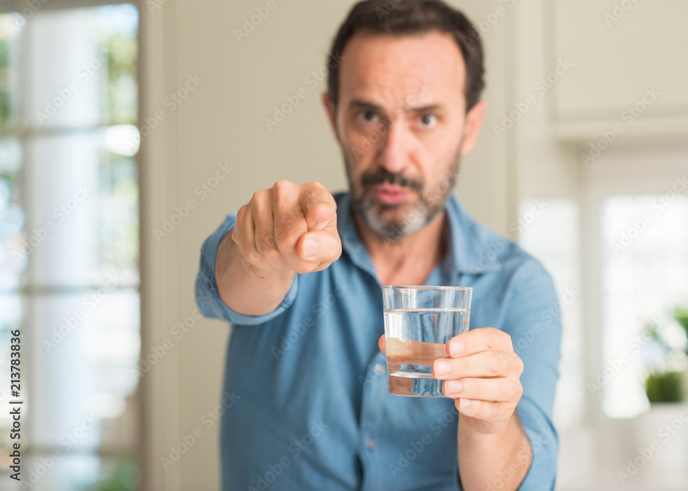 Middle age man drinking a glass of water pointing with finger to the camera and to you, hand sign, positive and confident gesture from the front Middle age man drinking a glass of water pointing with finger to the camera and to you, hand sign, positive and confident gesture from the front