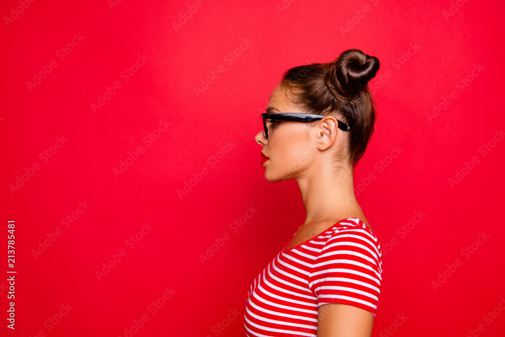Half-faced side profile view portrait of serious and confident young woman in striped shirt and spectacles isolated on red vivid background with copy space Half-faced side profile view portrait of serious and confident young woman in striped shirt and spectacles isolated on red vivid background with copy space