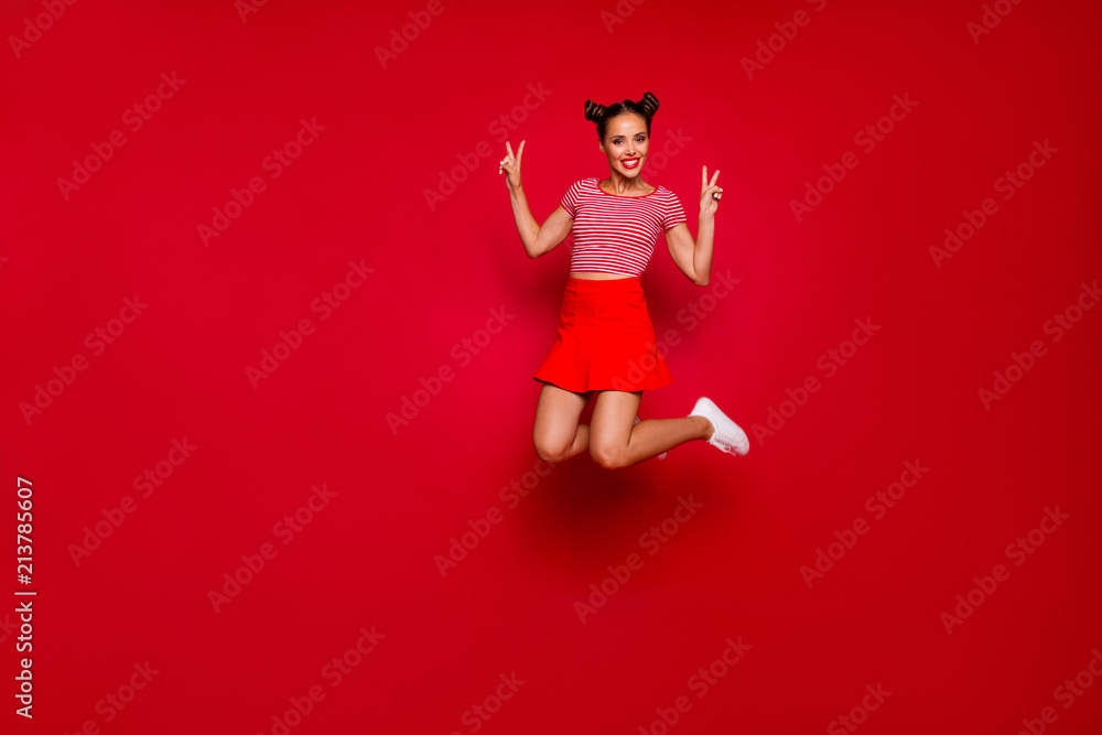 Full-length full-size view of jumping laughing and pretty woman dressed in colourful bright clothes shows a v-sign isolated on red background. Joy fun concept Full-length full-size view of jumping laughing and pretty woman dressed in colourful bright clothes shows a v-sign isolated on red background. Joy fun concept