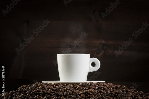 White cup of steaming coffee on heap of roasted beans