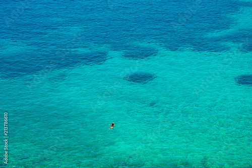 A man is swimming into the endless crystal clear turquoise waters of Vaporia region in Syros greek island, Cyclades, Greece. 