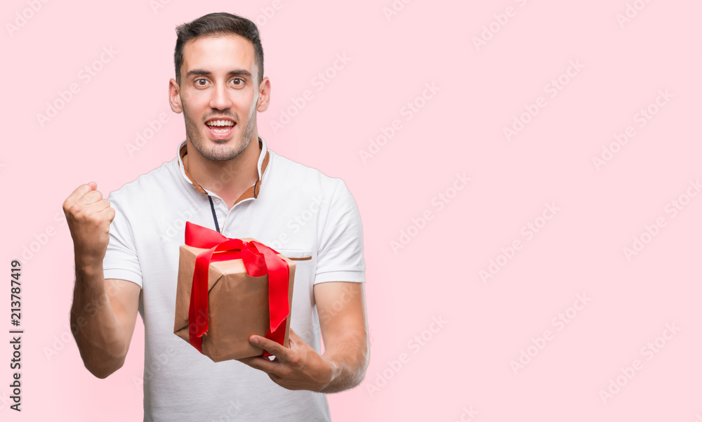 Handsome young man giving a present screaming proud and celebrating victory and success very excited, cheering emotion Handsome young man giving a present screaming proud and celebrating victory and success very excited, cheering emotion