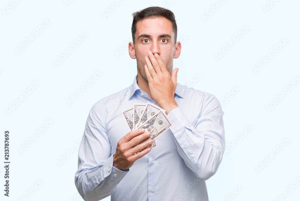 Handsome young man holding money cover mouth with hand shocked with shame for mistake, expression of fear, scared in silence, secret concept Handsome young man holding money cover mouth with hand shocked with shame for mistake, expression of fear, scared in silence, secret concept