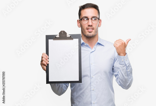 Handsome young business man showing a clipboard pointing with hand and finger up with happy face smiling