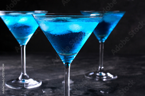 Three glasses of blue cold  martini cocktail with ice and clear dew drops on  glass on a gray concrete background , closeup shot