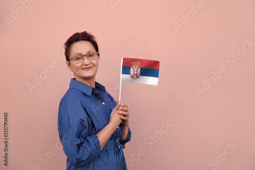 Serbia flag. Woman holding Serbian flag. Nice portrait of middle aged lady 40 50 years old with a national flag over pink wall background outdoors