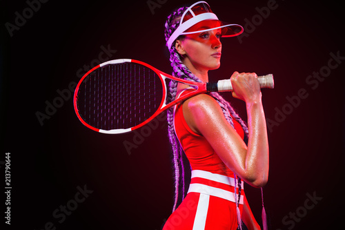 Tennis player. Beautiful woman athlete with racket in red costume and hat isolated on black background. Fashion and sport concept. © Mike Orlov
