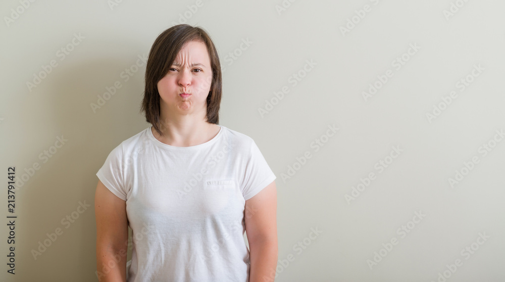 Down syndrome woman standing over wall puffing cheeks with funny face. Mouth inflated with air, crazy expression. Down syndrome woman standing over wall puffing cheeks with funny face. Mouth inflated with air, crazy expression.