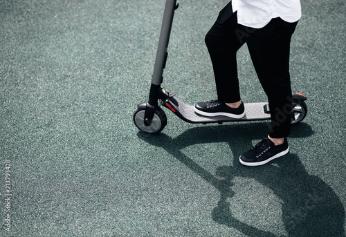 Legs of a man in stylish outfit stand on electric scooter on the street photo