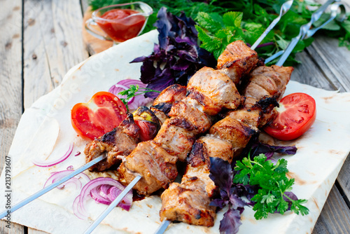 Barbecue. Juicy skewers of pork on pita bread. Decorated with herbs, tomatoes, pickled onion and basil, there is a red sauce next to it.