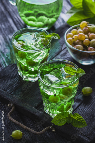 green gooseberry cocktail with ice and fresh mint on a black wooden table. refreshing summer drink