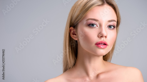 attractive young blonde woman looking at camera isolated on grey