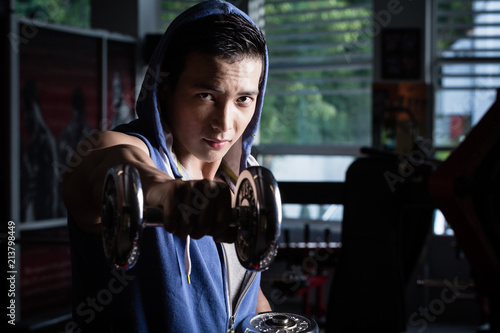 Young man wearing hoodie sweater reaching out with his hand holding a dumb-bell in gym