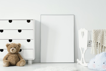Mockup of white empty poster between cradle and teddy bear in kid's room interior. Real photo