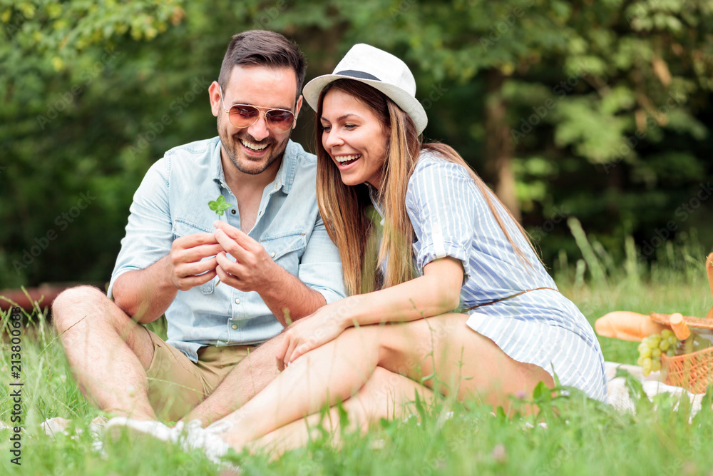 Beautiful young couple making a wish after finding four leaf clover while enjoying picnic in a park. Love and tenderness, dating, romance, lifestyle concept