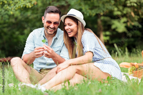 Obraz na płótnie Beautiful young couple making a wish after finding four leaf clover while enjoying picnic in a park. Love and tenderness, dating, romance, lifestyle concept w salonie