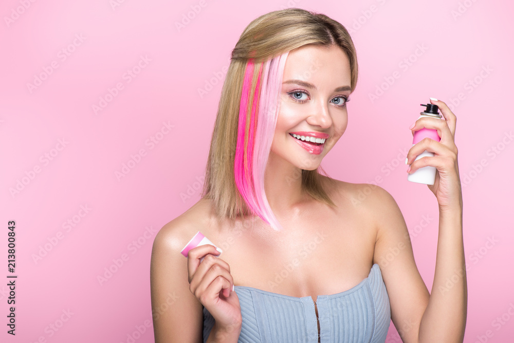 smiling young woman with colorful strands of hair and spray paint looking at camera isolated on pink smiling young woman with colorful strands of hair and spray paint looking at camera isolated on pink
