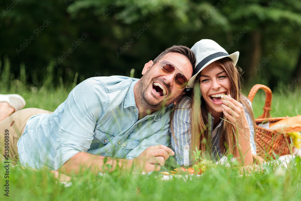 Beautiful happy young couple enjoying their time together, having relaxing picnic in a park. Lying close next to each other and laughing. Love and tenderness, dating, romance, lifestyle concept