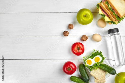 Lunch. Sandwich and fresh vegetables, bottle of water, nuts and fruits on white wooden background. Healthy eating concept. Top view with copy space