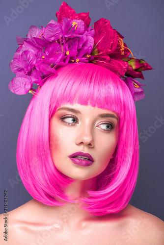attractive young woman with pink bob cut and flowers in hair looking away isolated on violet