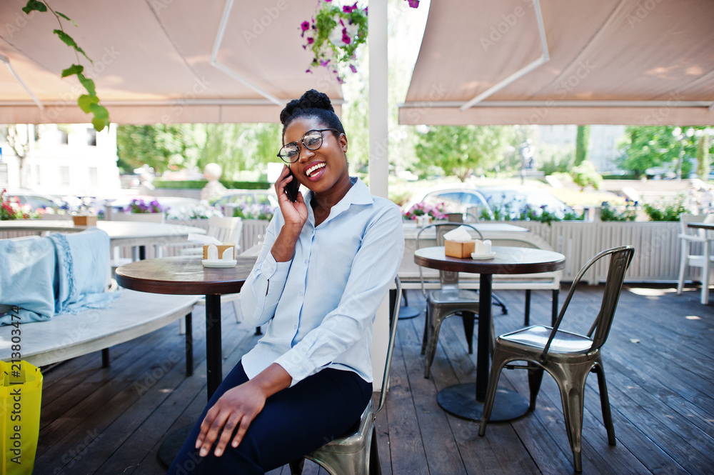 African american girl wear in glasses with mobile phone sitting at outdoor caffe. African american girl wear in glasses with mobile phone sitting at outdoor caffe.
