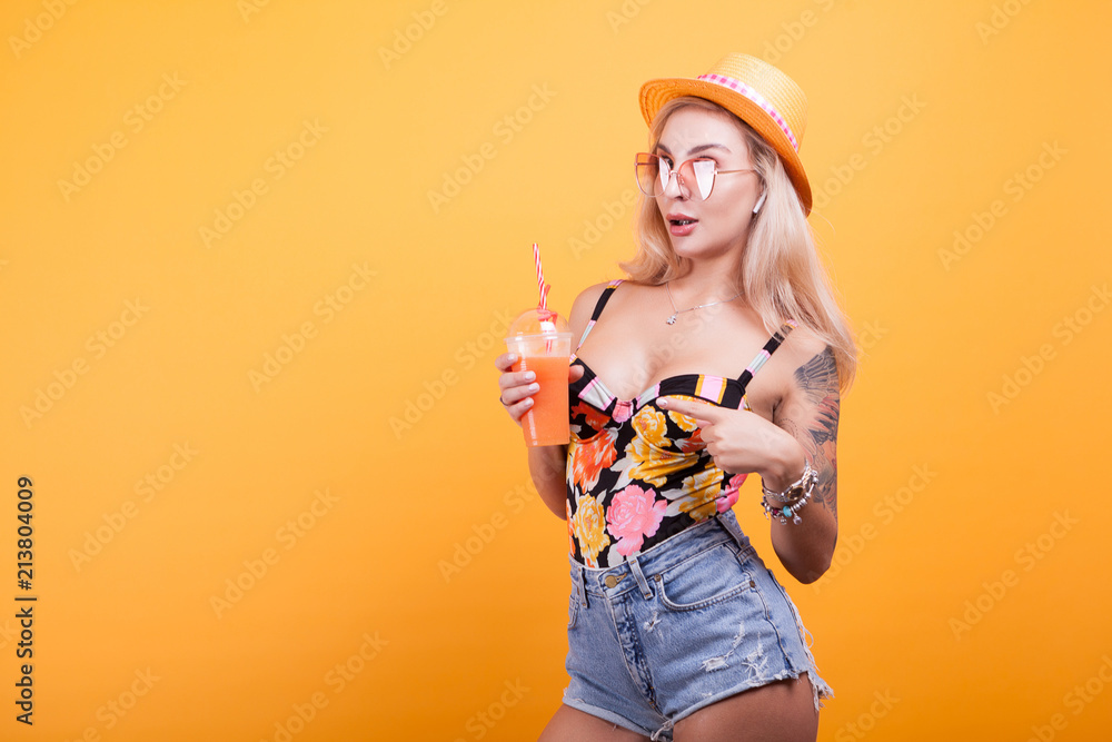 happy young woman looking at summer fresh orange juice thinking she's sexy in studio over yellow background happy young woman looking at summer fresh orange juice thinking she's sexy in studio over yellow background