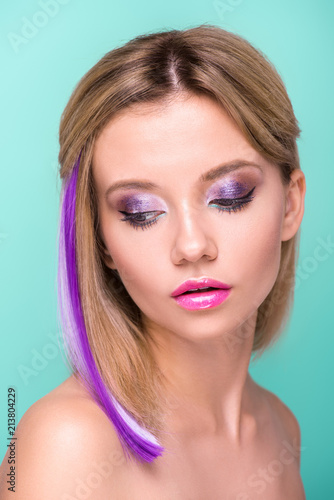 close-up portrait of attractive young woman with stylish makeup and purple hair strand isolated on blue