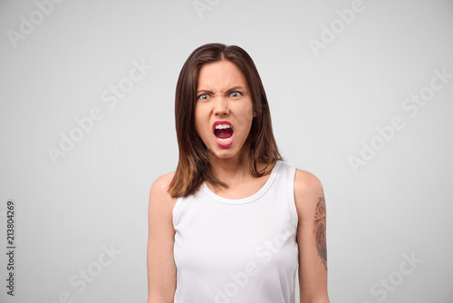 Furious angry woman screaming with rage and frustration. Negative human emotions, face expressions. Portrait of a frustrated angry woman screaming out loud out isolated on the gray background