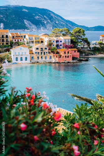 Fototapeta Naklejka Na Ścianę i Meble -  Beautiful colorful southern houses and blue bay of Mediterranean sea with some red flowers on foreground. Assos village in Kefalonia, Greece