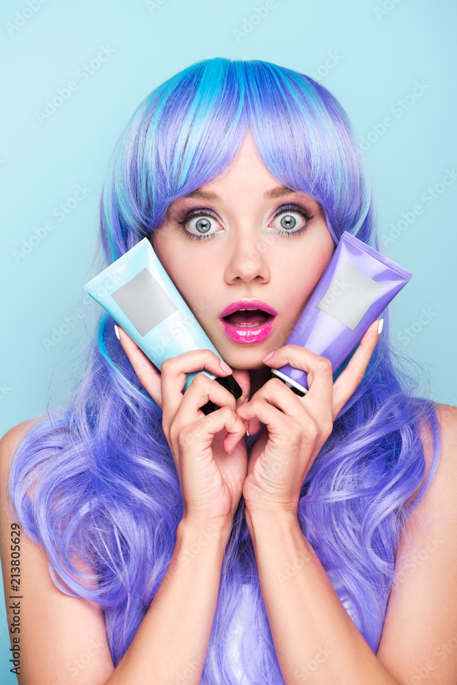 shocked young woman with tubes of coloring hair tonics isolated on blue shocked young woman with tubes of coloring hair tonics isolated on blue