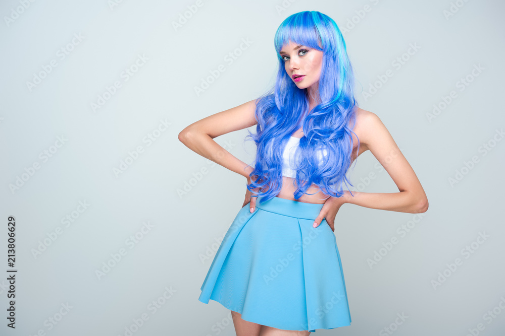 beautiful young woman with bright blue hair standing with arms akimbo and looking at camera isolated on grey beautiful young woman with bright blue hair standing with arms akimbo and looking at camera isolated on grey