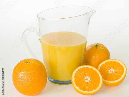 ein Glaskrug mit Orangensaft, davor liegen Orangen 