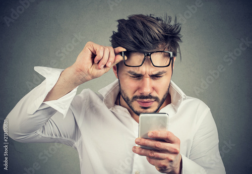Confused man reading phone with difficulties photo