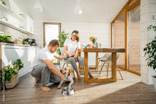 Young couple playing with dog during a breakfast in the dining room of their beautiful wooden country house