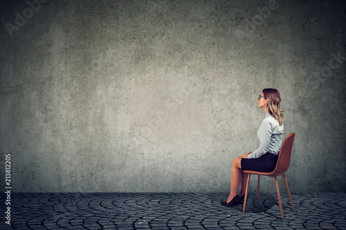 Business woman sitting on a chair in front of a wall and thinking