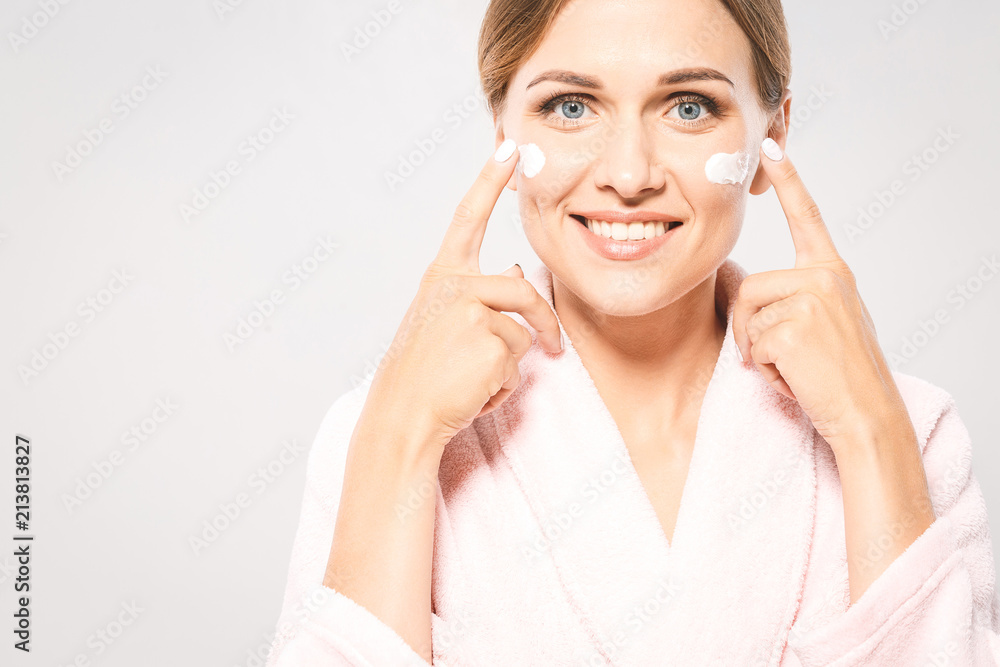 Portrait of young beautiful woman smiling while taking some facial cream isolated on white background with copy space. Portrait of young beautiful woman smiling while taking some facial cream isolated on white background with copy space.