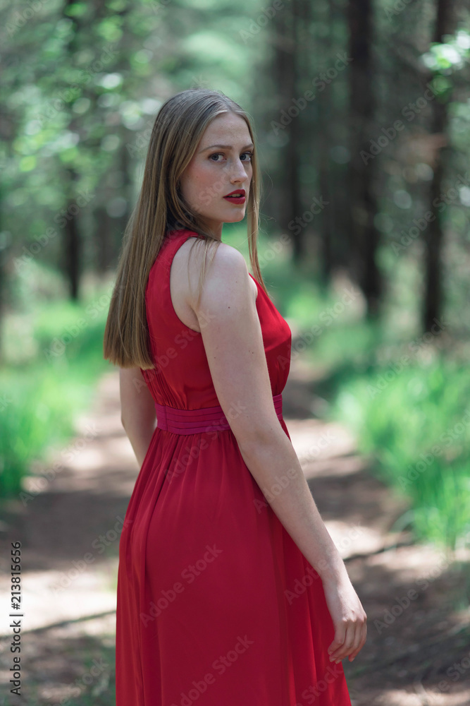 Blonde woman in red dress in forest looking over shoulder. Blonde woman in red dress in forest looking over shoulder.