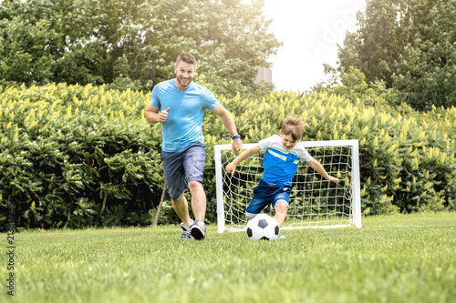 Man with child playing football outside on field © Louis-Photo