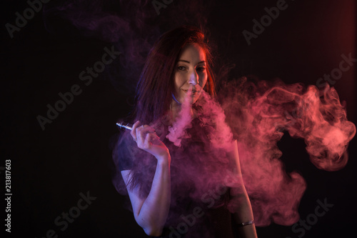 Portrait of asian woman smoking vape or e-cigarette in neon light at black background.