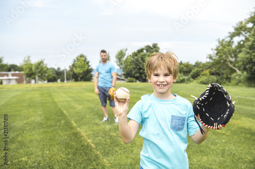 Wall Mural Handsome dad with his little cute sun are playing baseball on green grassy lawn
