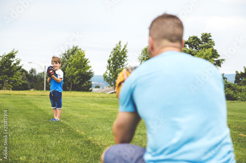 Canvas Print Handsome dad with his little cute sun are playing baseball on green grassy lawn